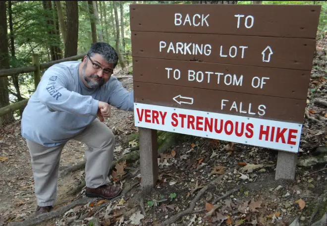 Man giving a thumbs down to a sign saying very strenuous hike.
